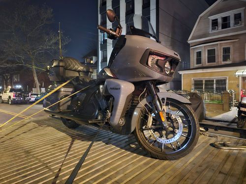 Gray motorcycle parked on a brick-paved street at night. Police tape in the background.