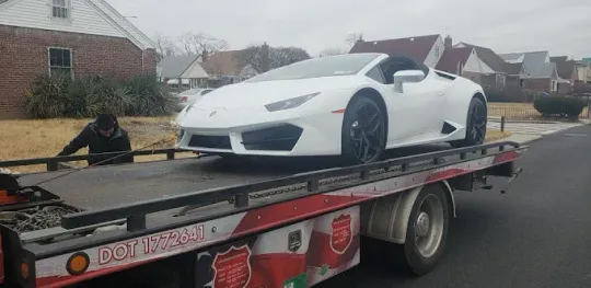 White Lamborghini convertible on a tow truck in a residential area.