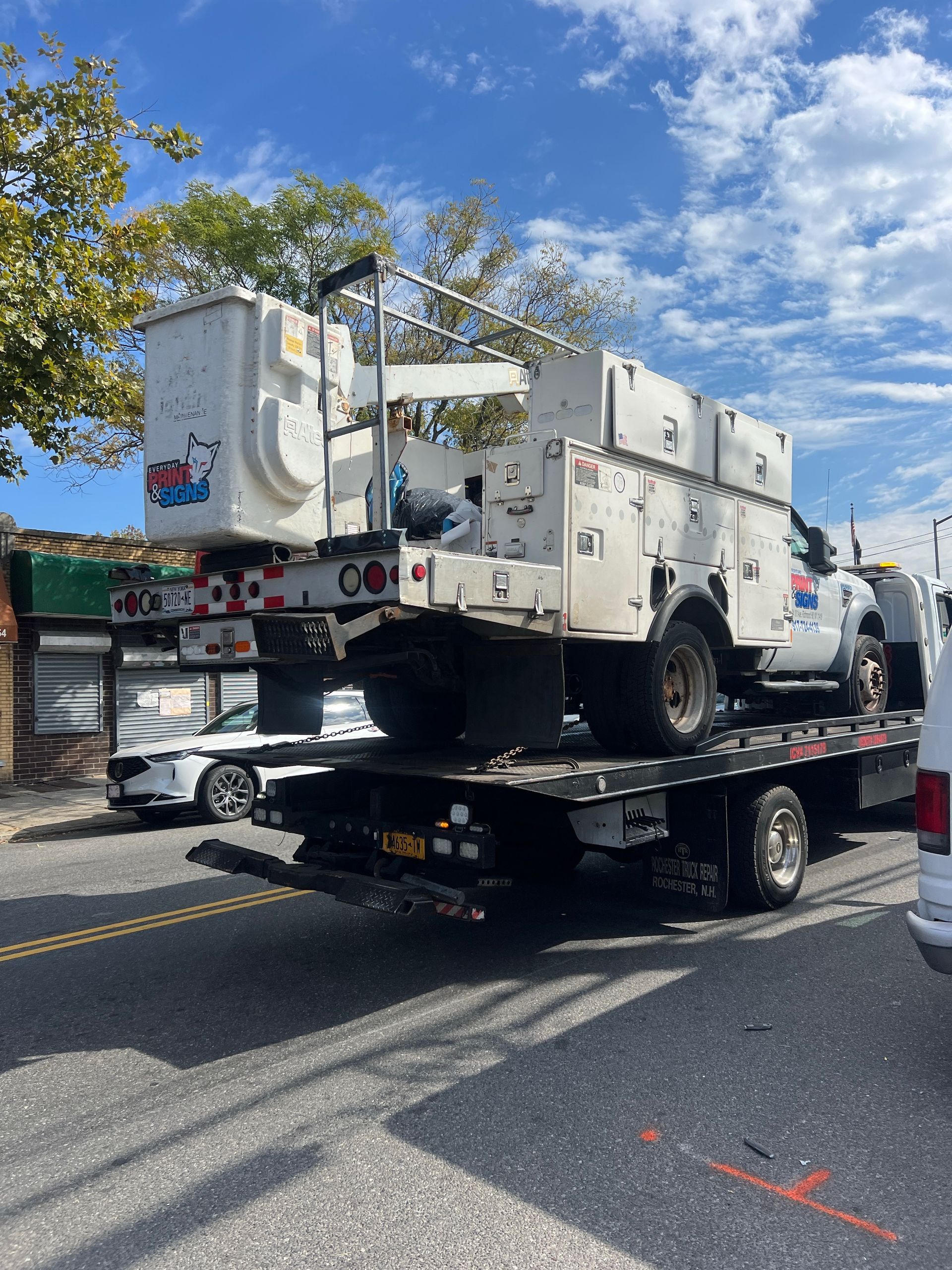 White utility truck on a flatbed tow truck on a city street with trees and blue sky