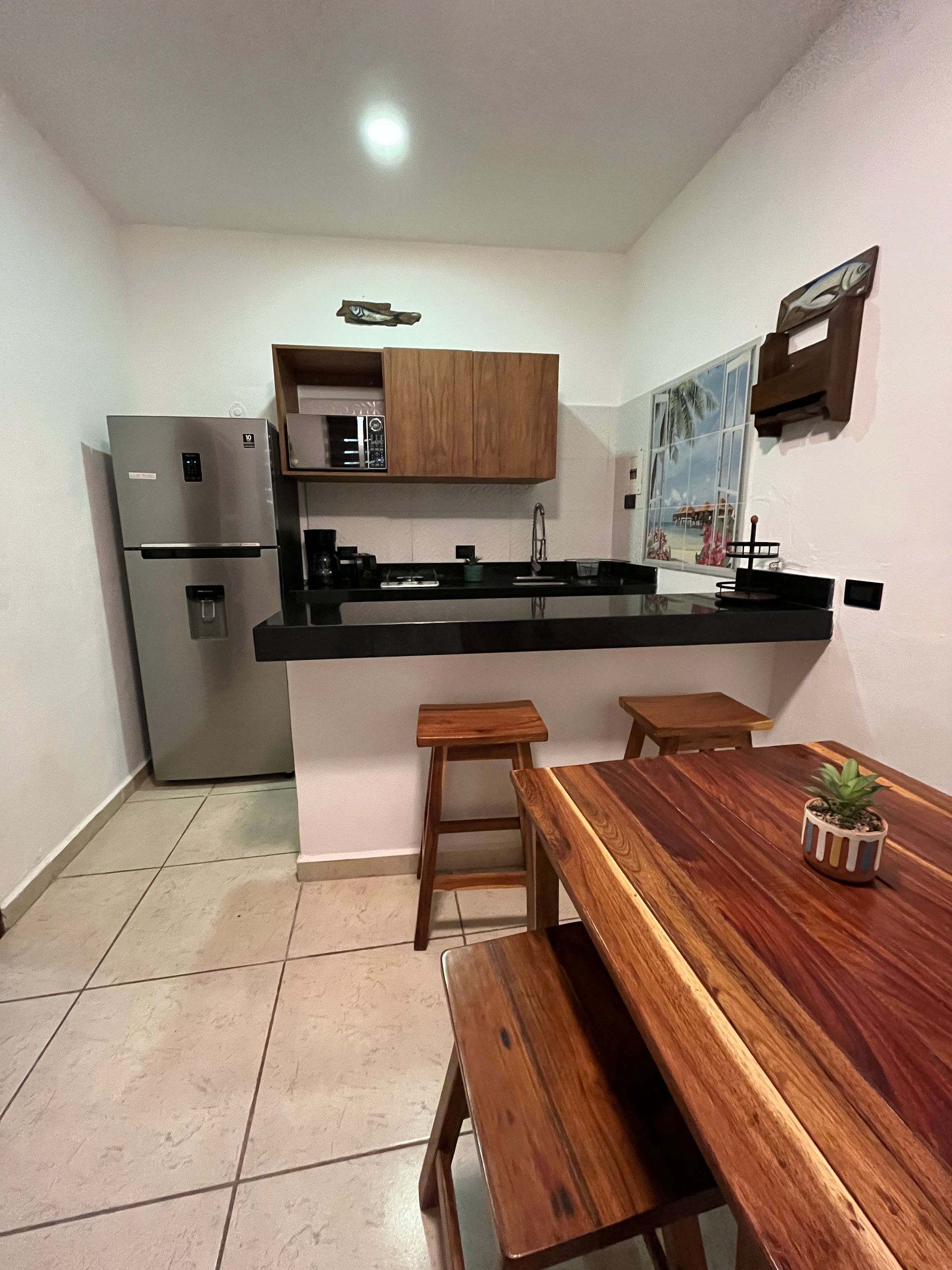 Cocina con gabinetes de madera, barra, refrigerador y mesa de comedor de madera.
