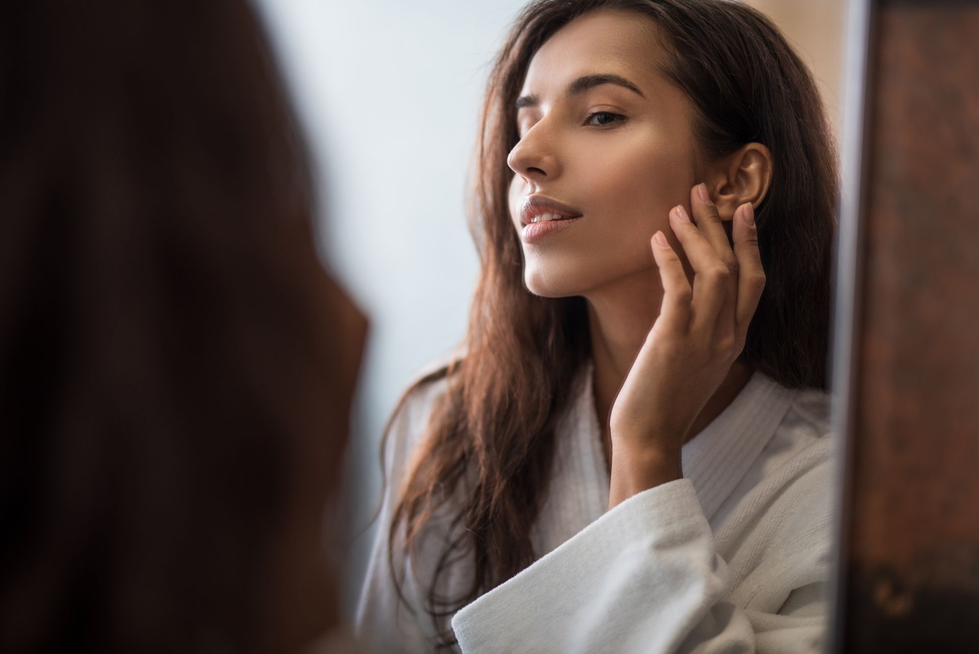 A woman is looking at her face in the mirror.