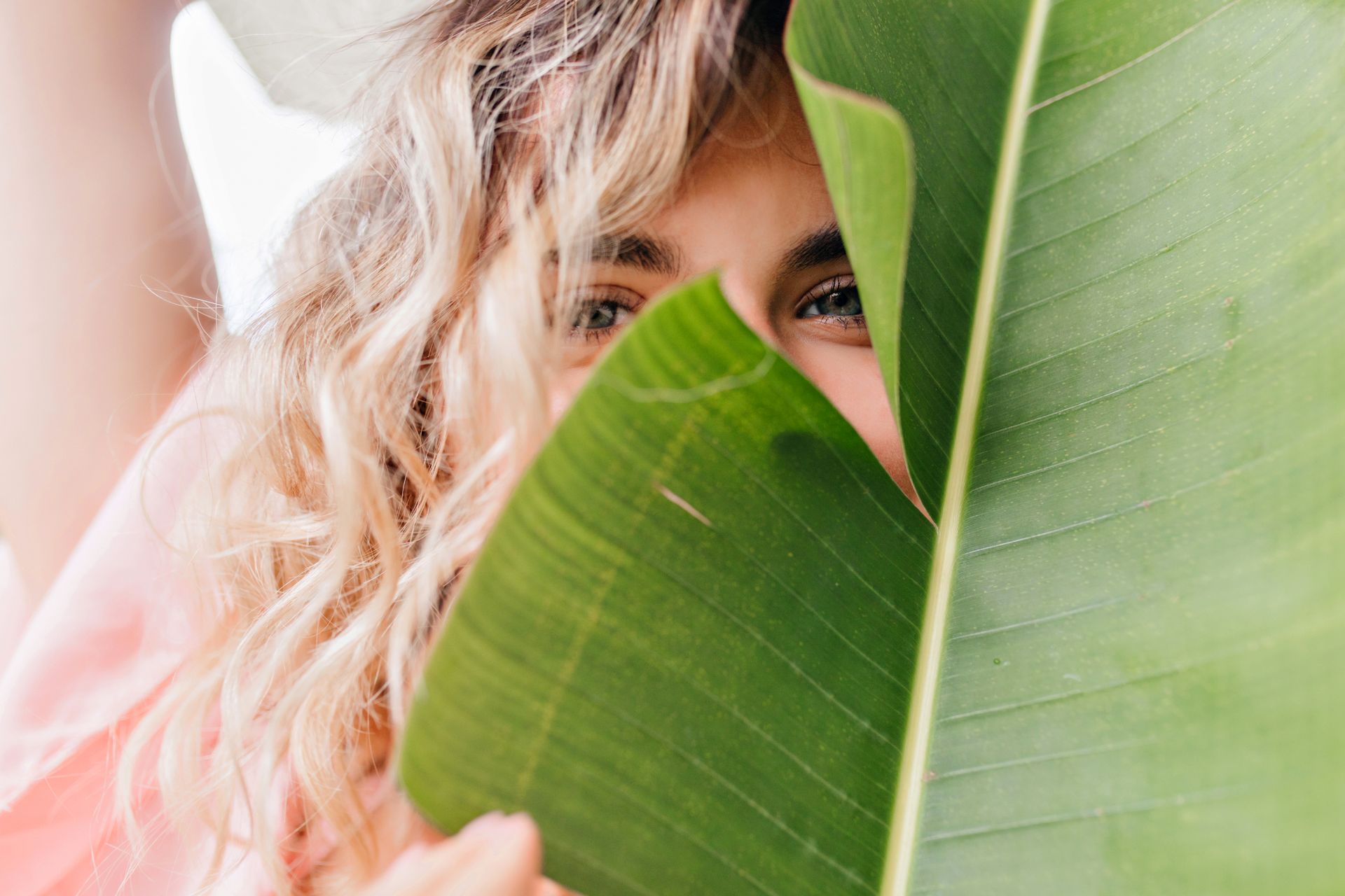 A woman is peeking out from behind a banana leaf.