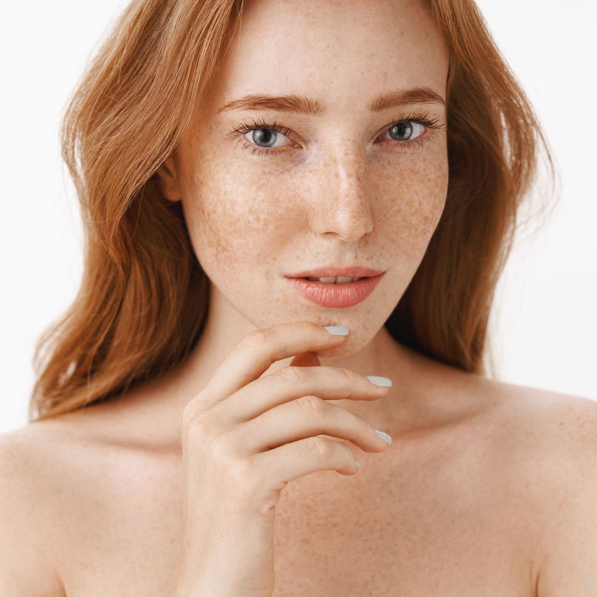 A woman with red hair and freckles is holding her hand to her face.