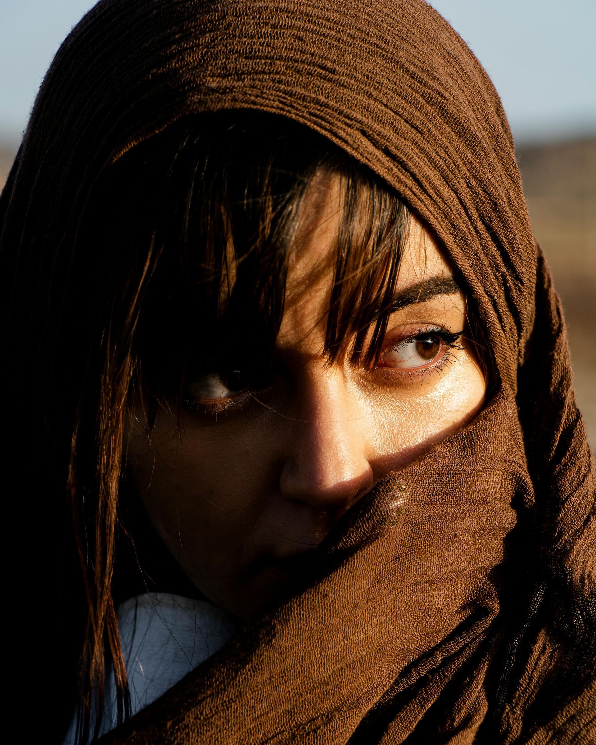 A woman covering her face with a brown scarf