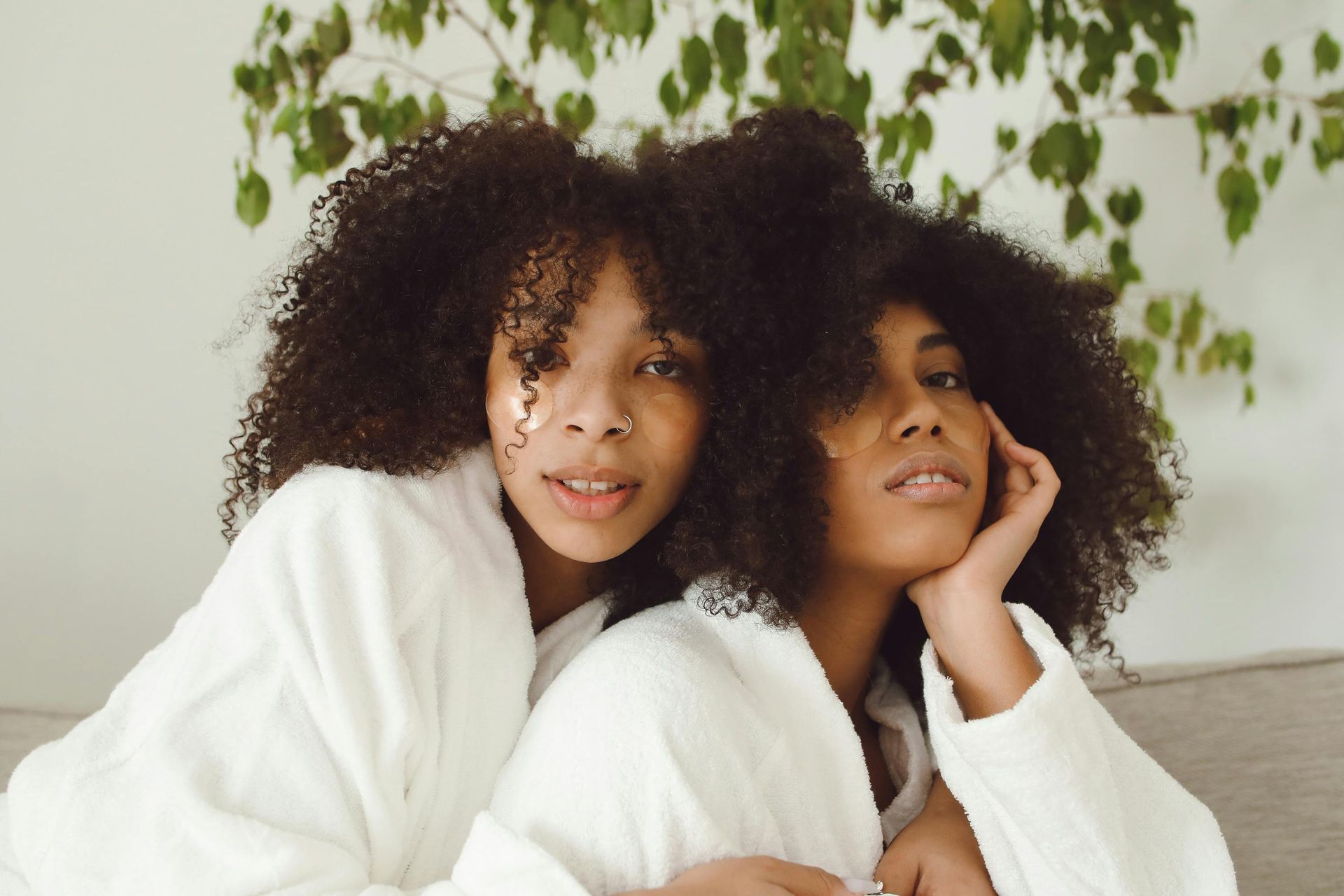 Two women with curly hair are sitting next to each other on a couch.