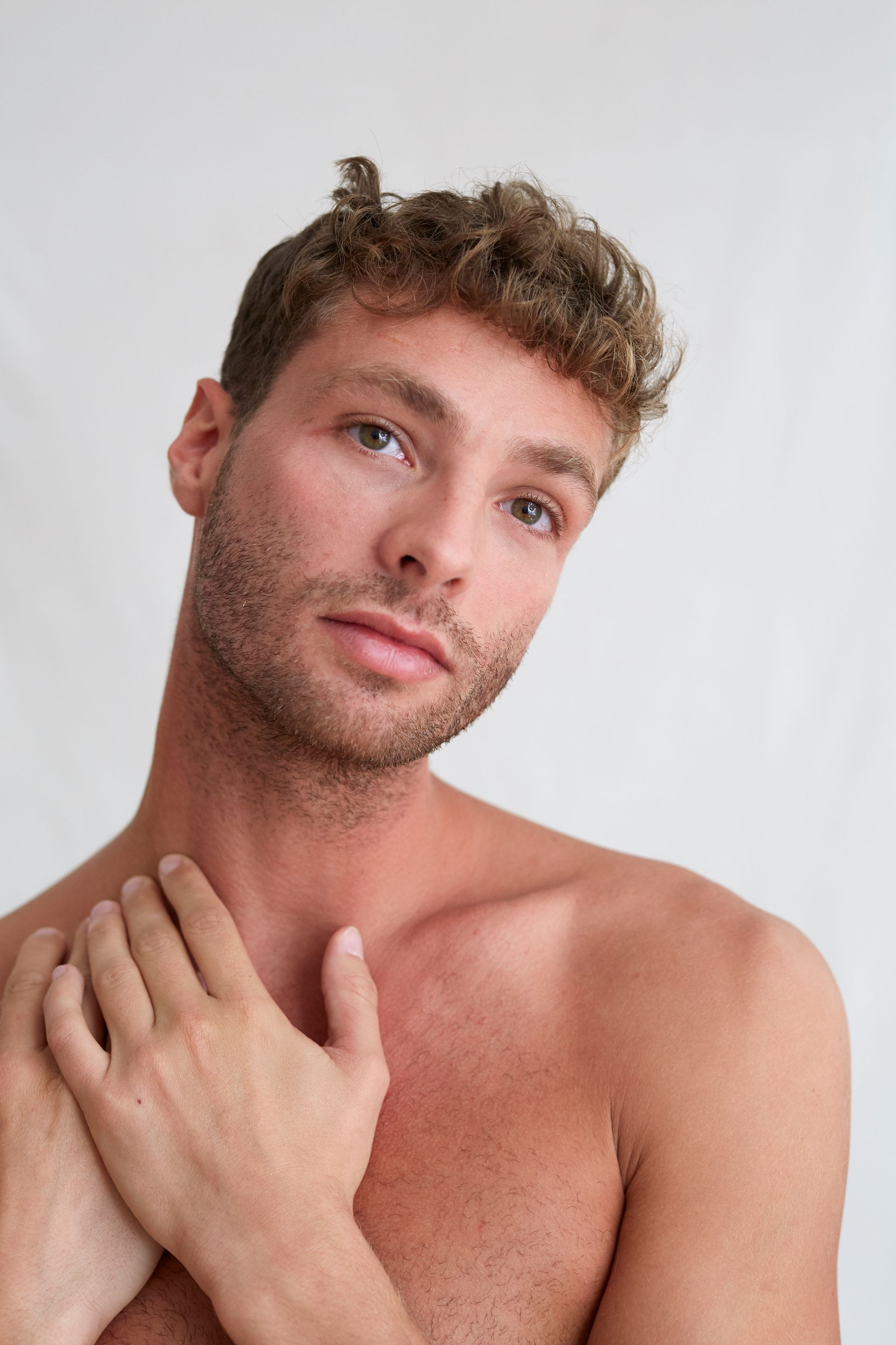 A shirtless man with a beard is holding his hands to his chest.