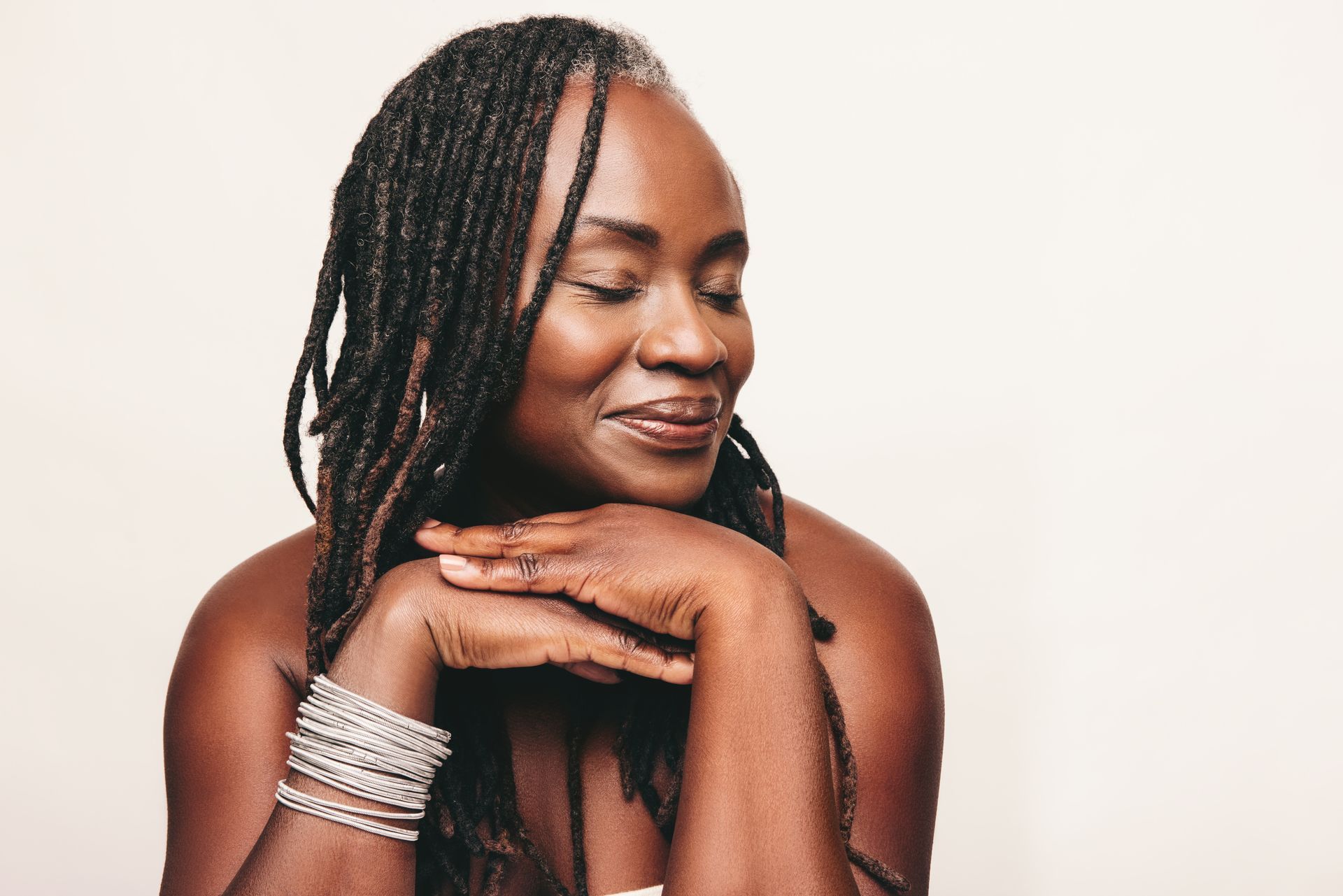 A woman with dreadlocks is smiling with her eyes closed and her hands on her face.