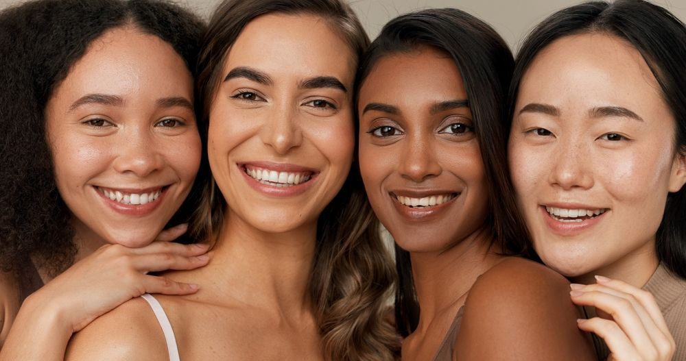 A group of women of different races are posing for a picture together and smiling.