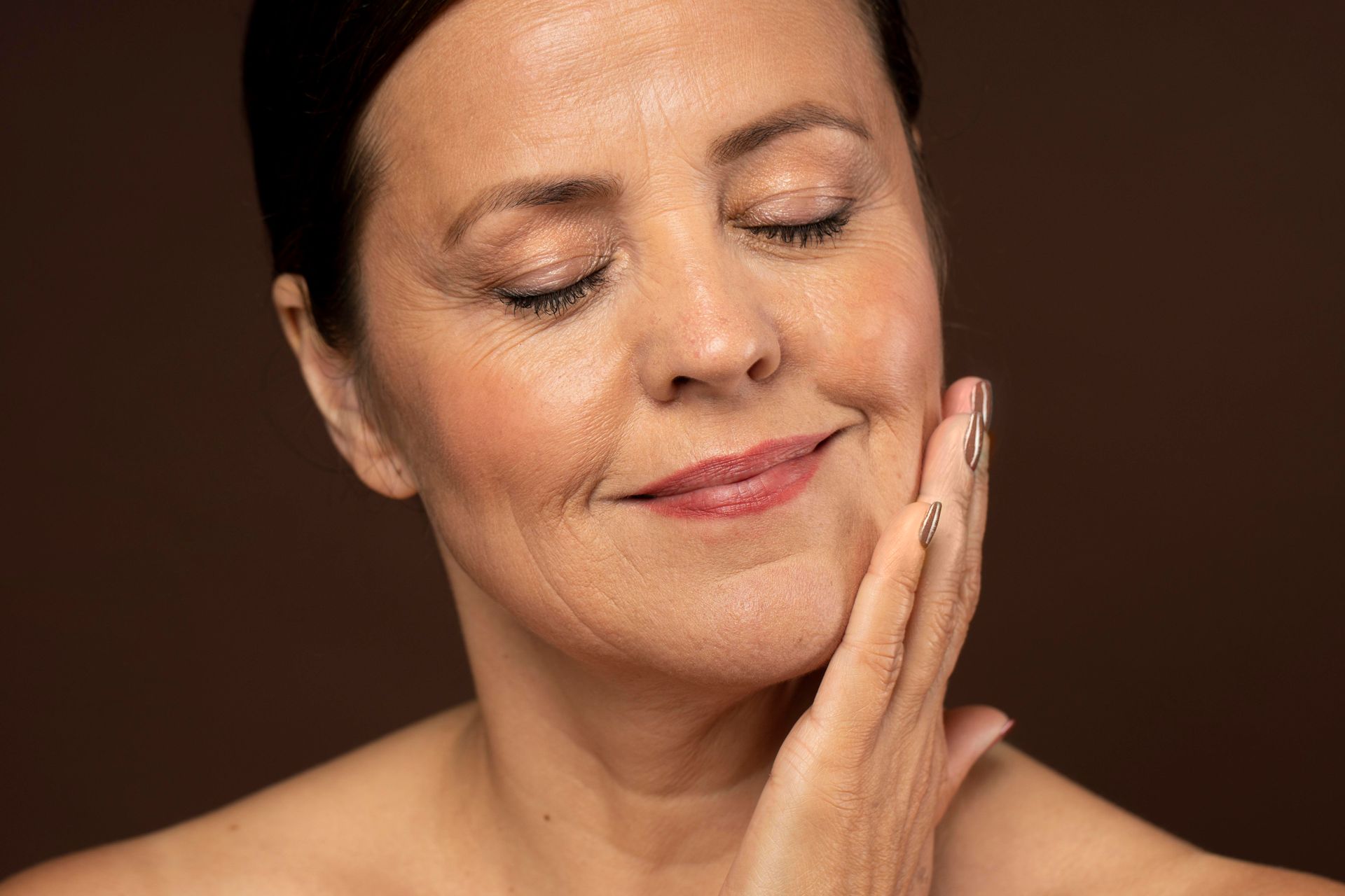 A woman is touching her face with her hands and smiling.