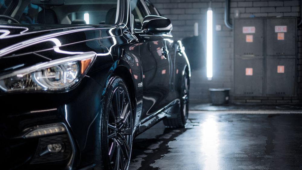 A black car is parked in a garage under a light.