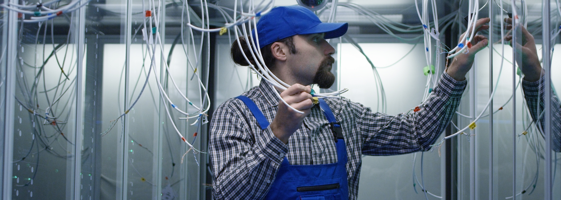 Picture of an IT technician amongst cables, looking perplexed
