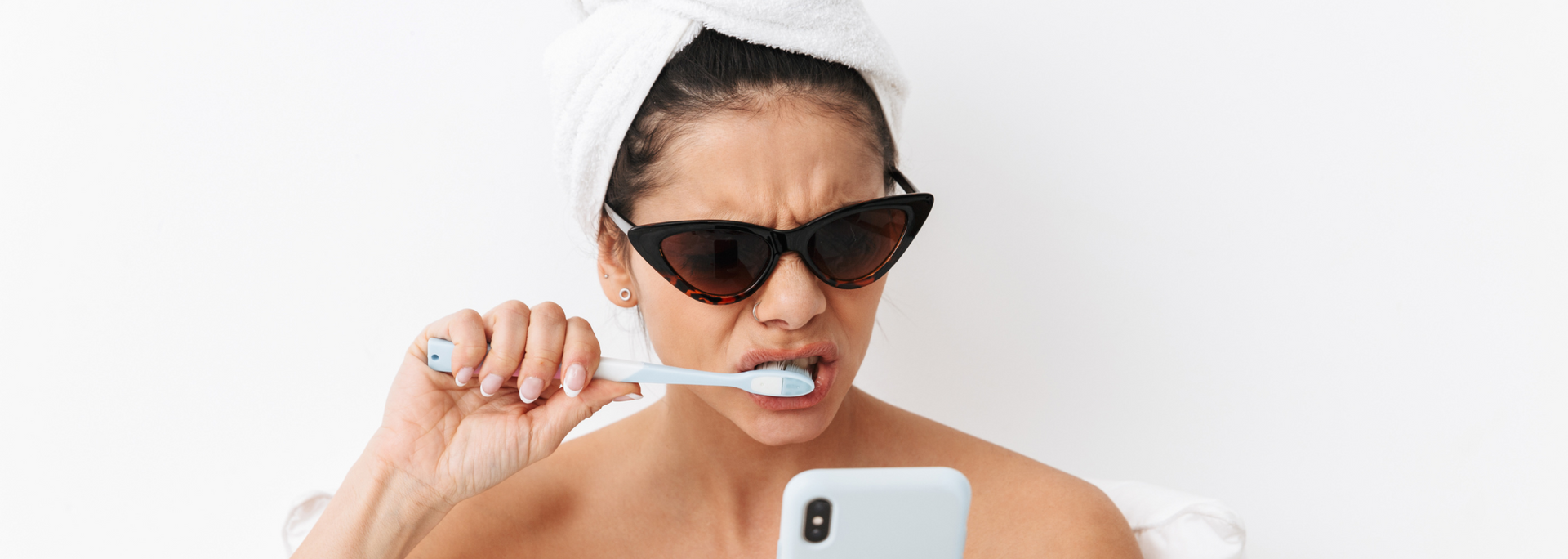 Picture of a woman brushing her teeth while looking at her phone.
