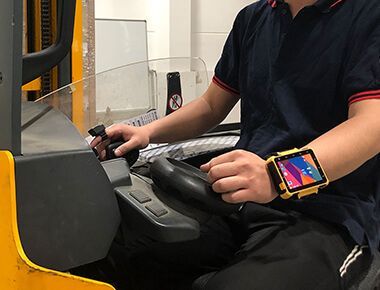 A man wearing a smart watch  W563 Wearable Computer is driving a forklift.
