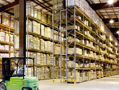 A green forklift is driving through a large warehouse filled with shelves and boxes.