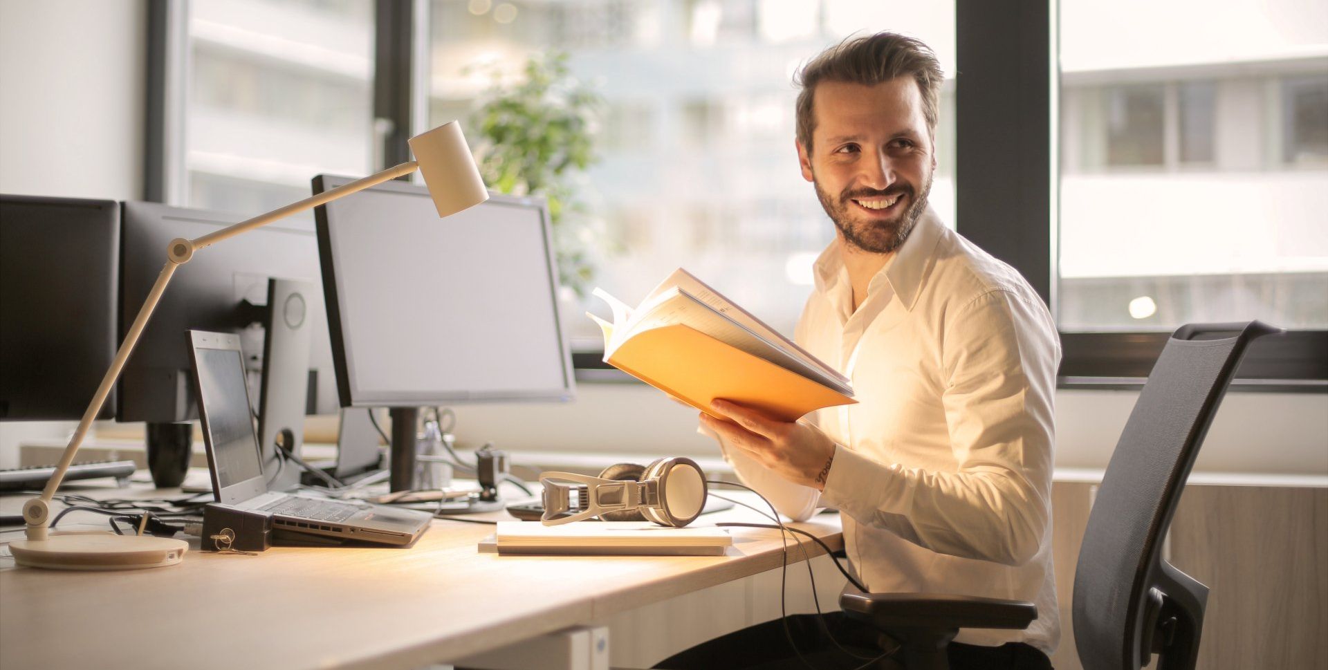 A man is sitting at a desk in an office holding a folder.