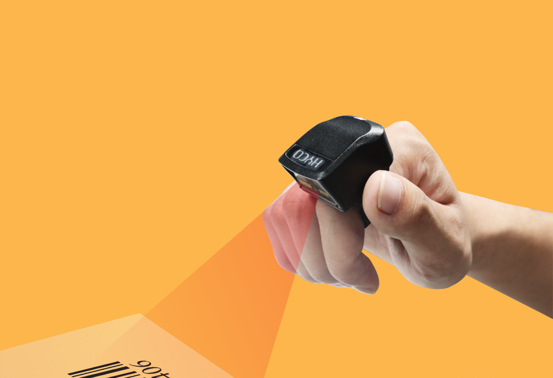 A person is holding a barcode scanner (Hyco Ring Scanner) in their hand.