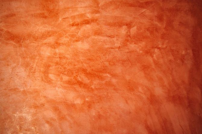 A textured, mottled surface with various shades of orange and terracotta, resembling rustic plaster or painted concrete.