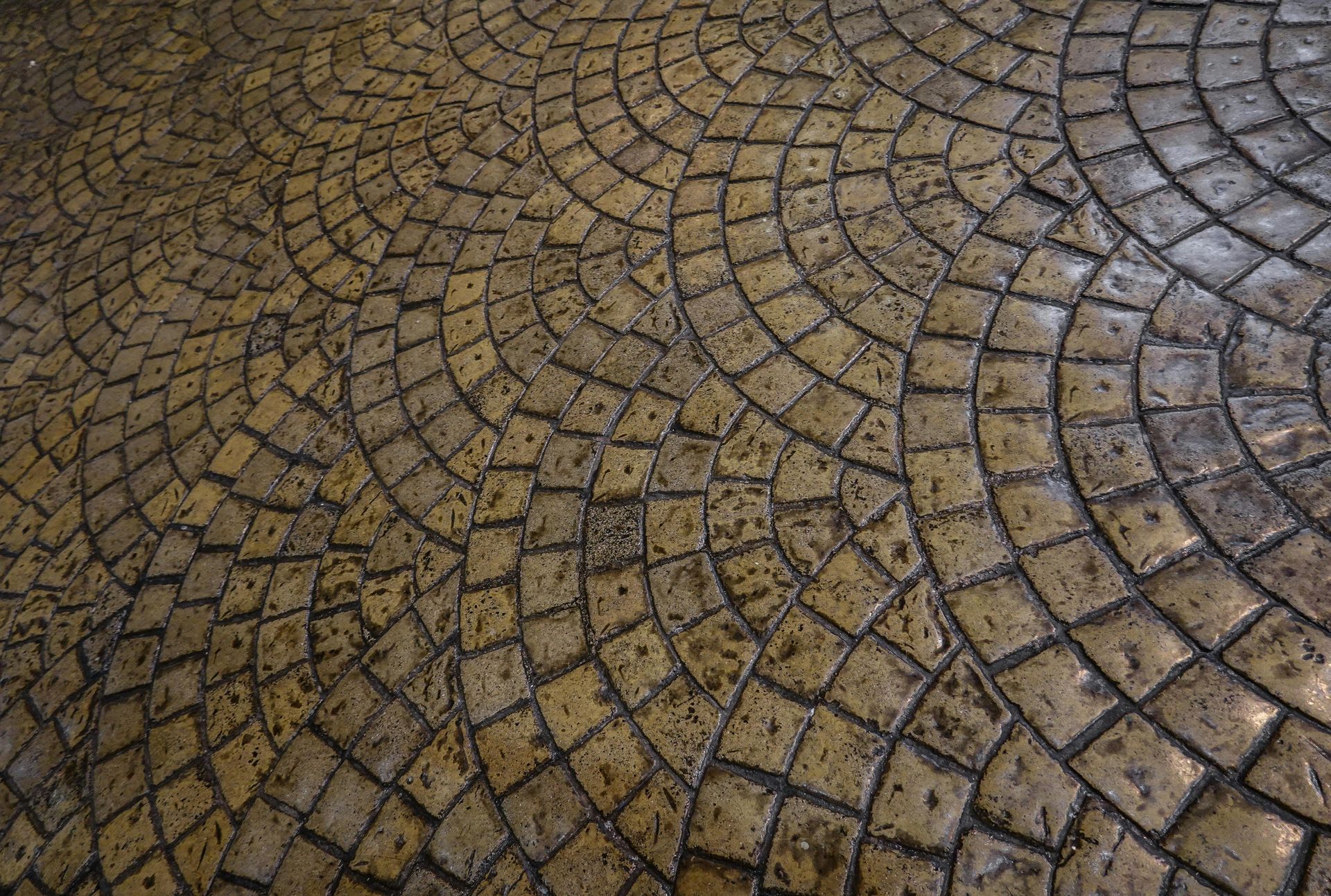 A textured pavement made of small, fan-patterned, weathered yellow-brown cobblestones.
