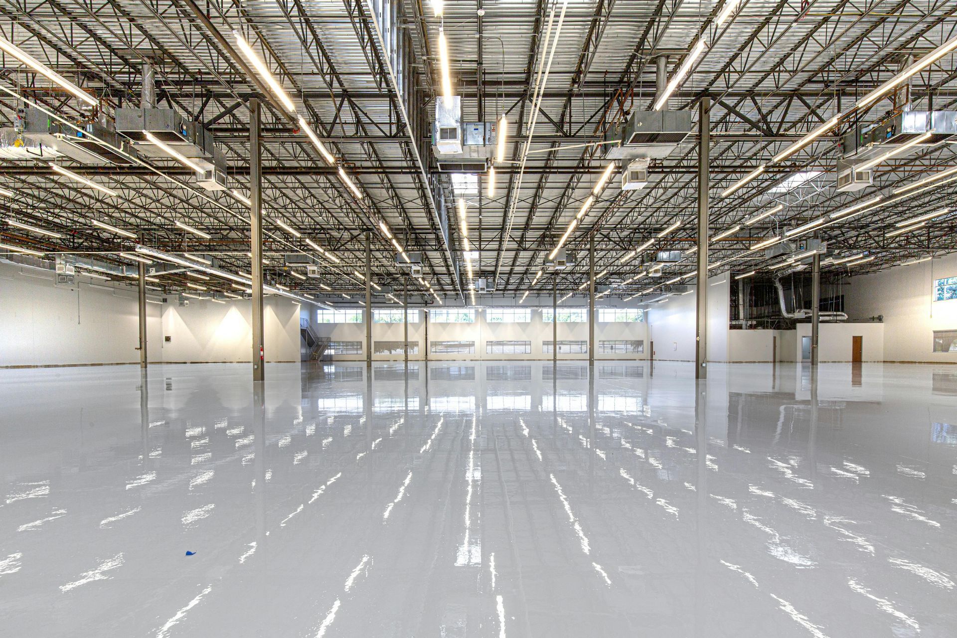 A wide-angle, interior view of a large, empty industrial warehouse with high ceilings, exposed trusses, and glossy floors.