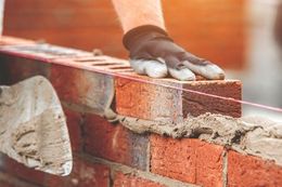 A gloved hand laying bricks on a wall with a string guide, construction site.