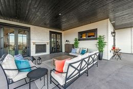 Patio with outdoor furniture, fireplace, and black ceiling. Beige walls, gray floor, and blue, orange, and white cushions.