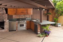 Outdoor kitchen with brick, wood cabinets, stainless steel appliances, and concrete countertop.