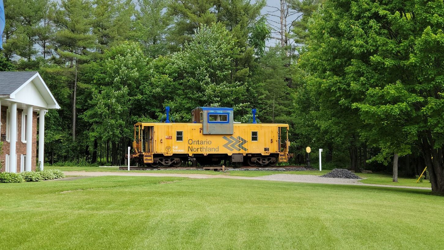A yellow train car is parked in the grass in front of a house.