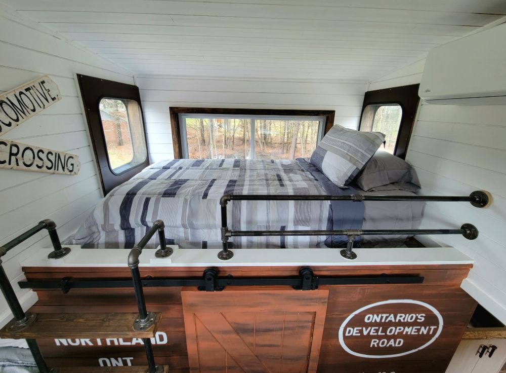 A bed is sitting on top of a wooden platform in a tiny house.