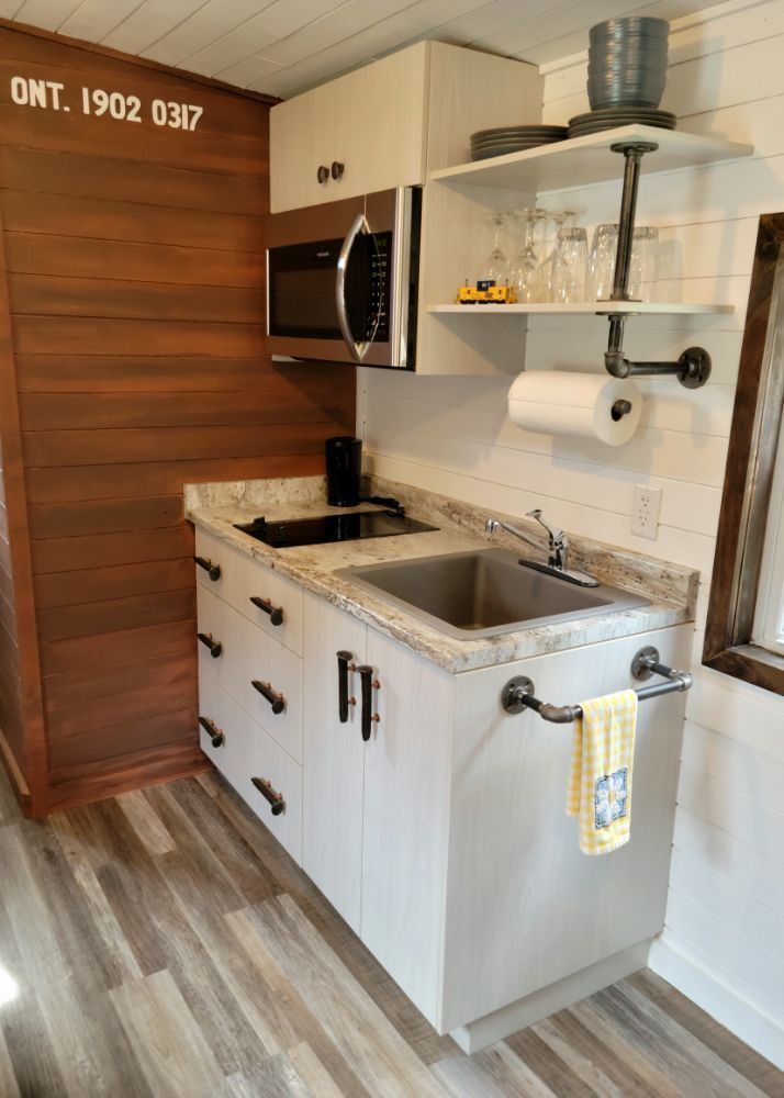 A small kitchen with a sink , microwave , and shelf.