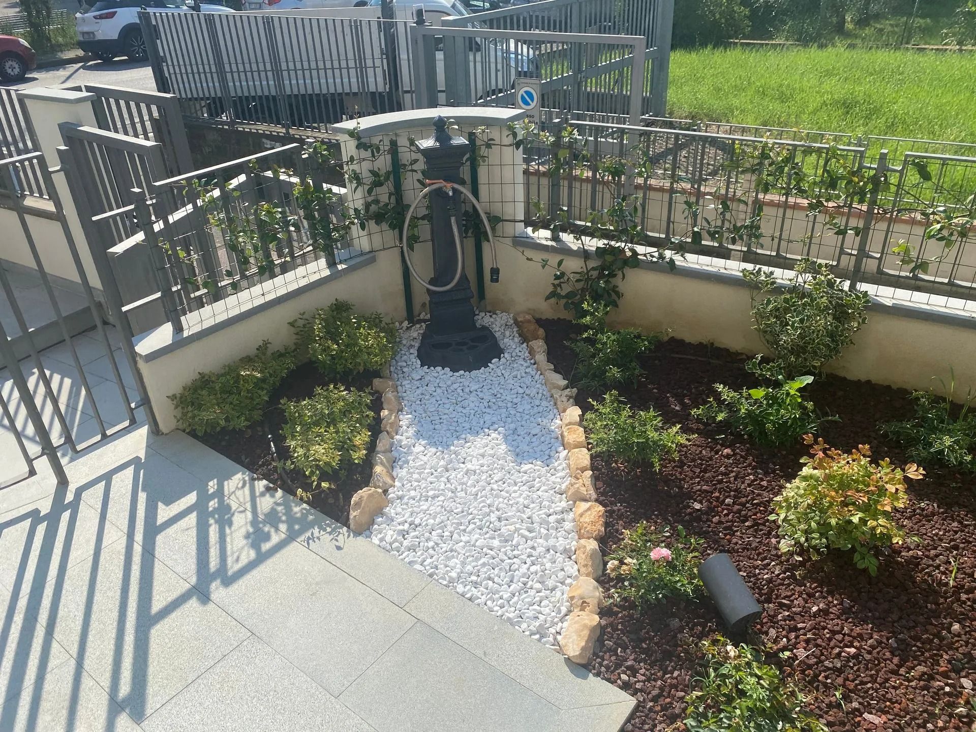 Sentiero del giardino con pietre bianche che conduce a una scultura nera con piante su entrambi i lati e una recinzione in ferro battuto.