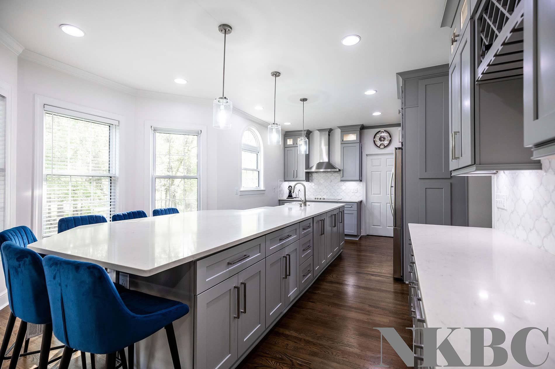 A kitchen with gray cabinets , white counter tops , and blue chairs.