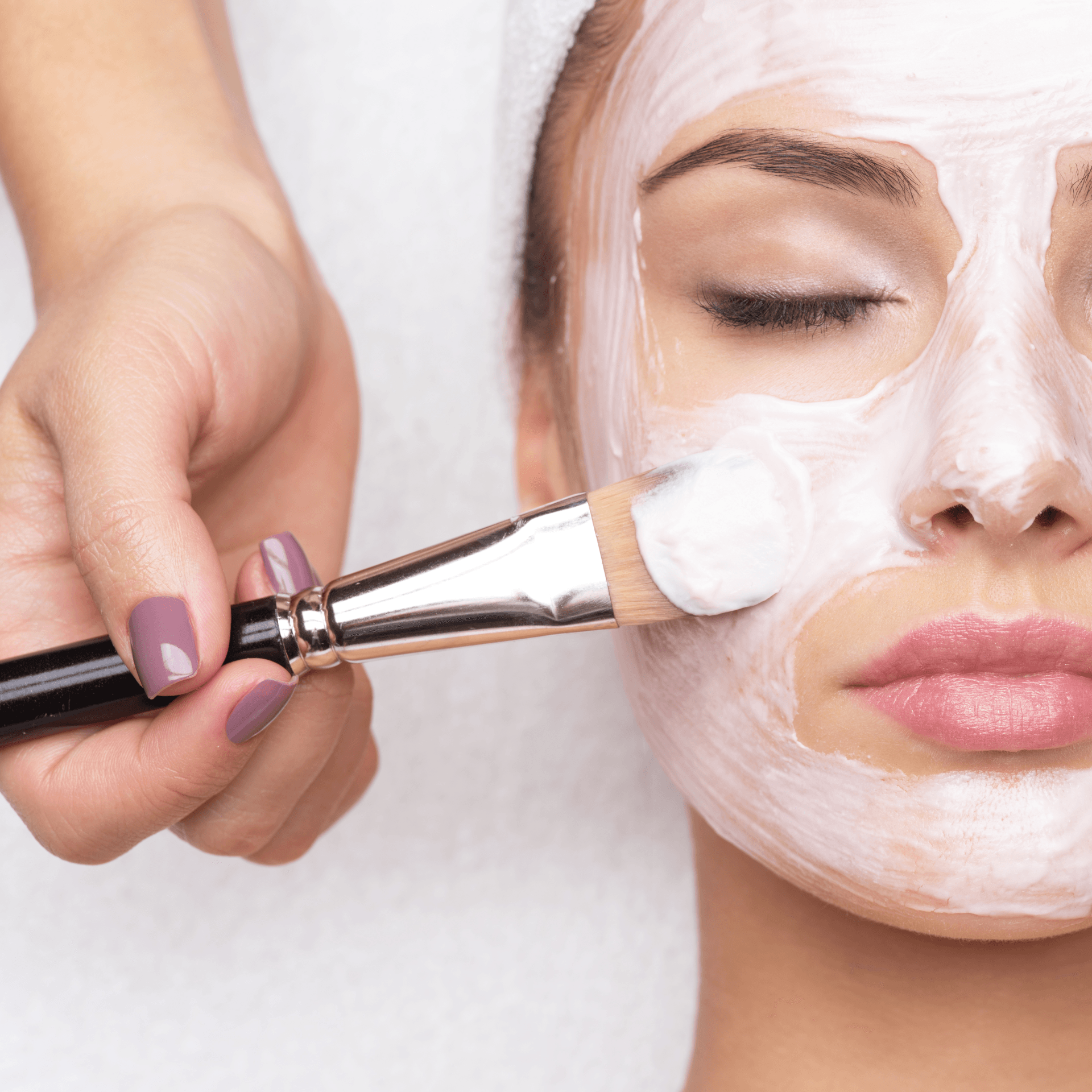 A woman is getting a white mask on her face.