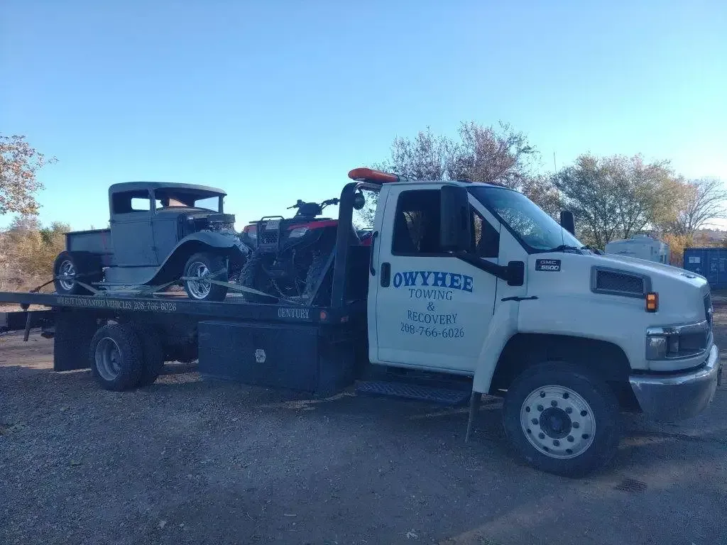 Gray classic car being towed on a white tow truck. Outdoors on a sunny day.