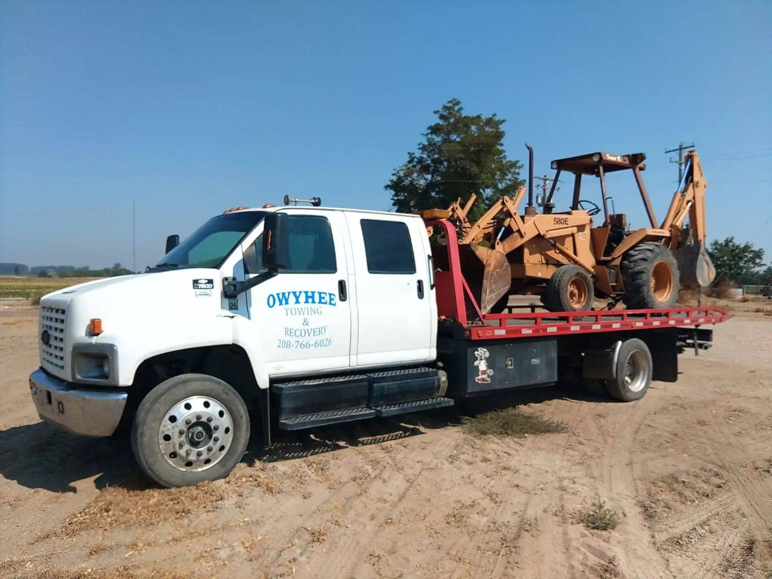 White tow truck transporting an orange backhoe on a sunny day.