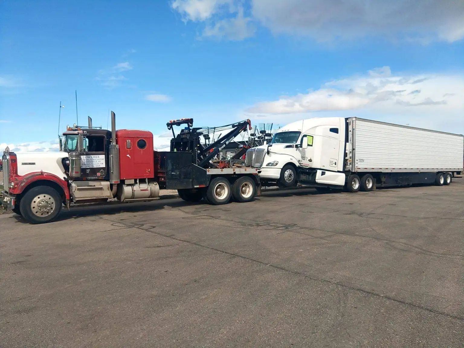 Tow truck towing a semi-truck with a white trailer on a road under a blue sky.