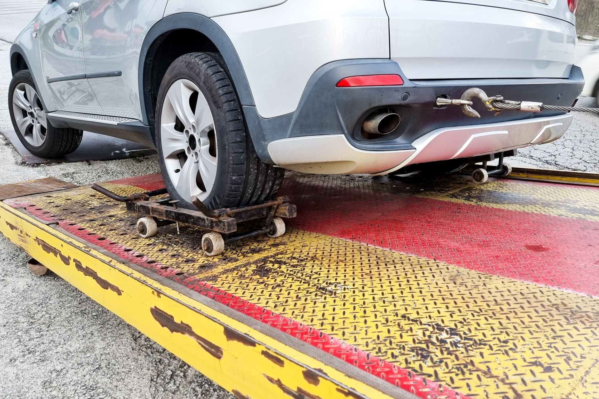 Silver SUV on a tow truck, rear tire on a dolly. The truck bed is yellow and red.