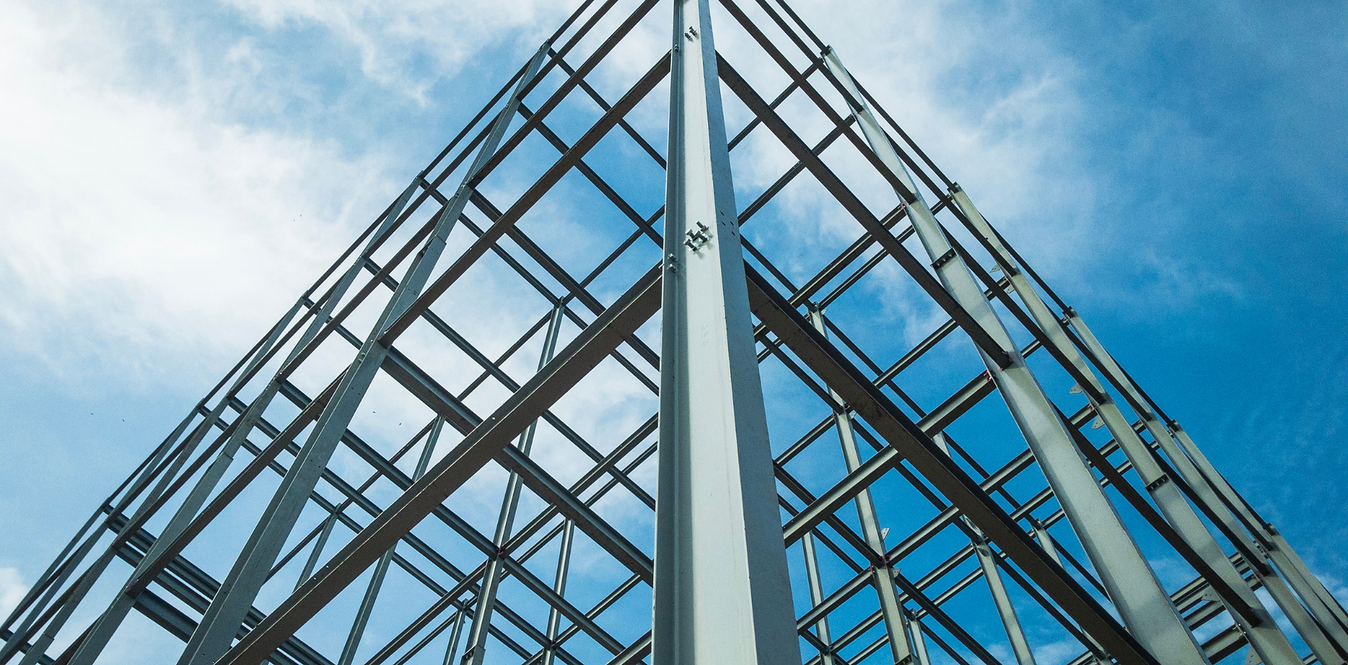 Low-angle view of a metal and glass building structure against a cloudy blue sky.