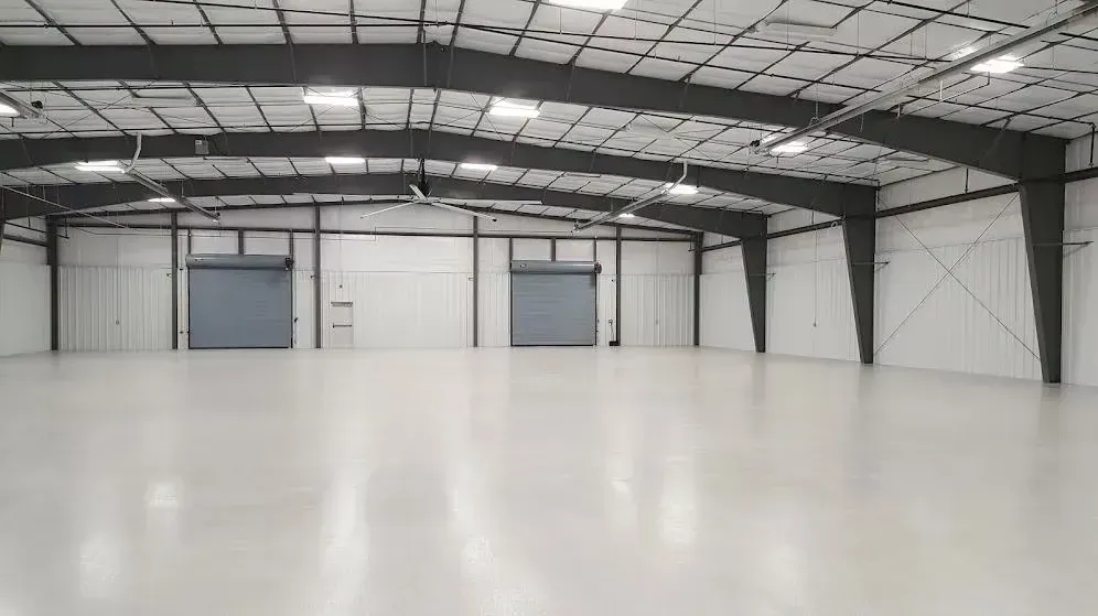 Empty warehouse interior, white walls, gray beams, large roller doors, and a smooth, reflective floor.