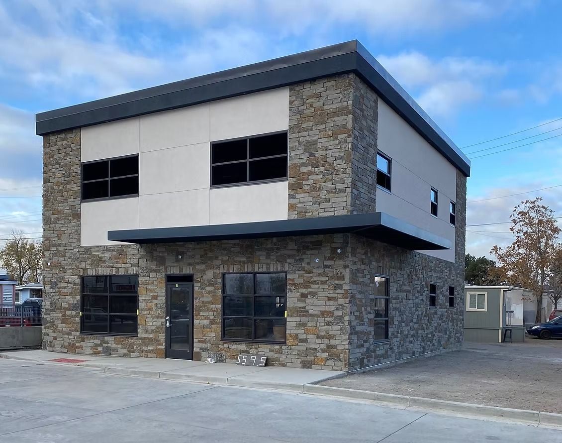 Two-story commercial building with stone facade and dark trim. Features include large windows and a small awning.