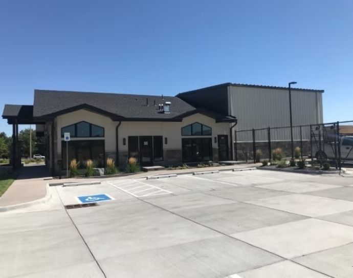 Building with parking lot; accessible parking space. Dark roof, tan and grey facade, metal storage area.