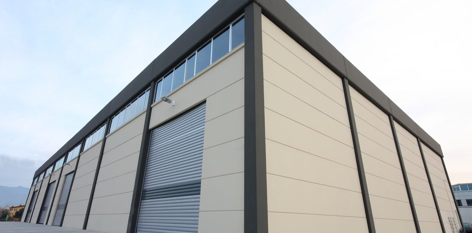 Exterior view of a modern industrial building with a roll-up door and a dark roof.