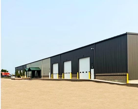 Exterior of a long, industrial building with multiple loading dock doors. Gray and black metal exterior, clear sky.