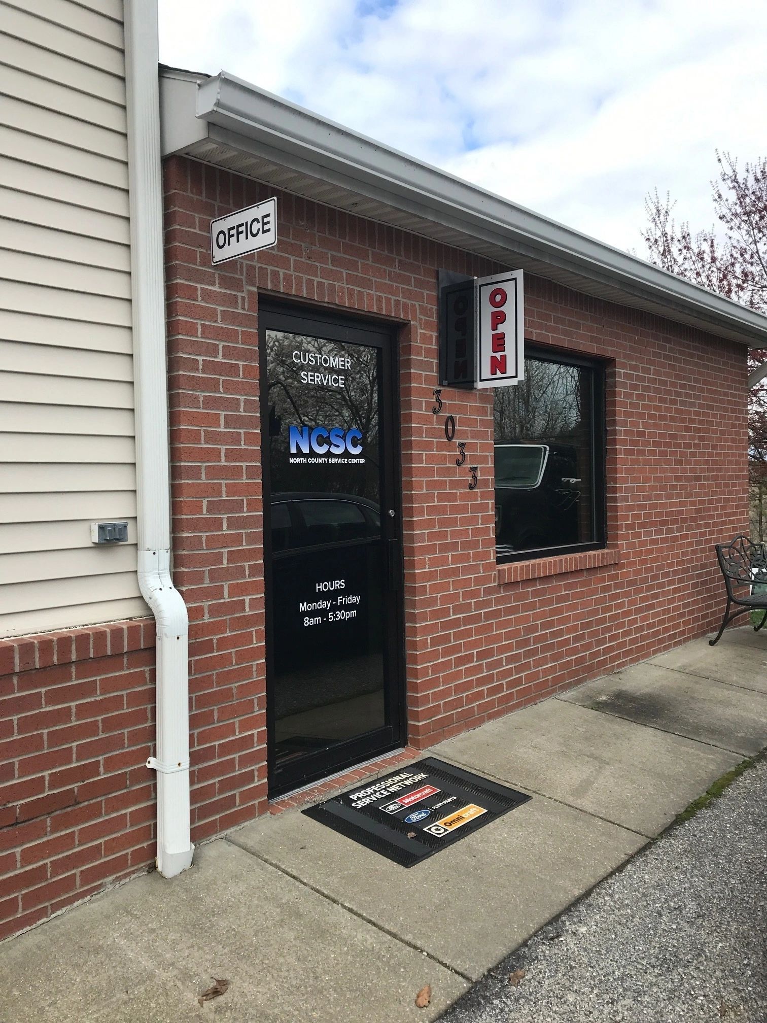A brick building with a black door and a black mat on the sidewalk. | North County Service Center