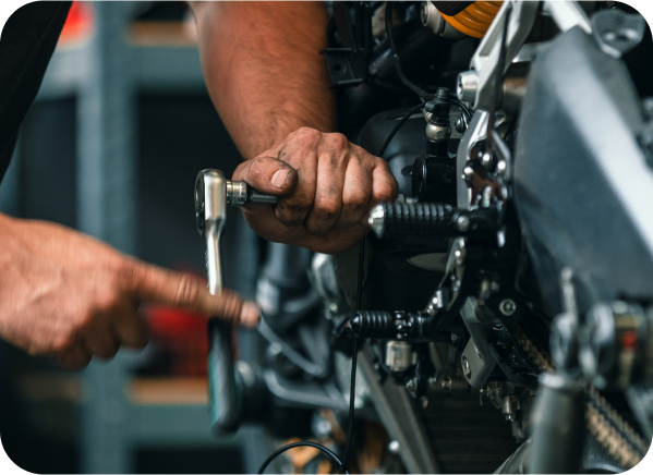 A man is working on a motorcycle with a wrench. | North County Service Center