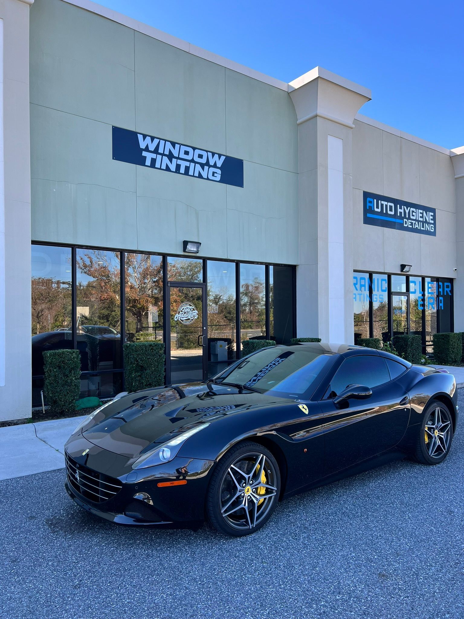 Black Ferrari parked in front of a business with window tinting services.