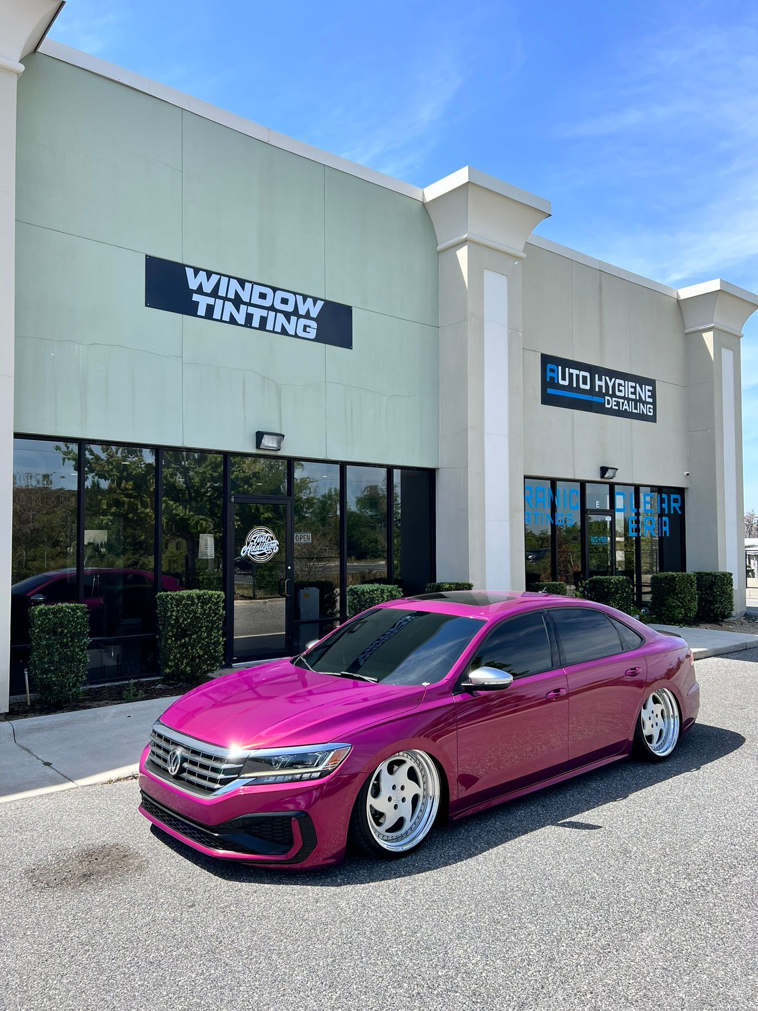 Purple car parked in front of a window tinting business. Blue sky, sunny day.