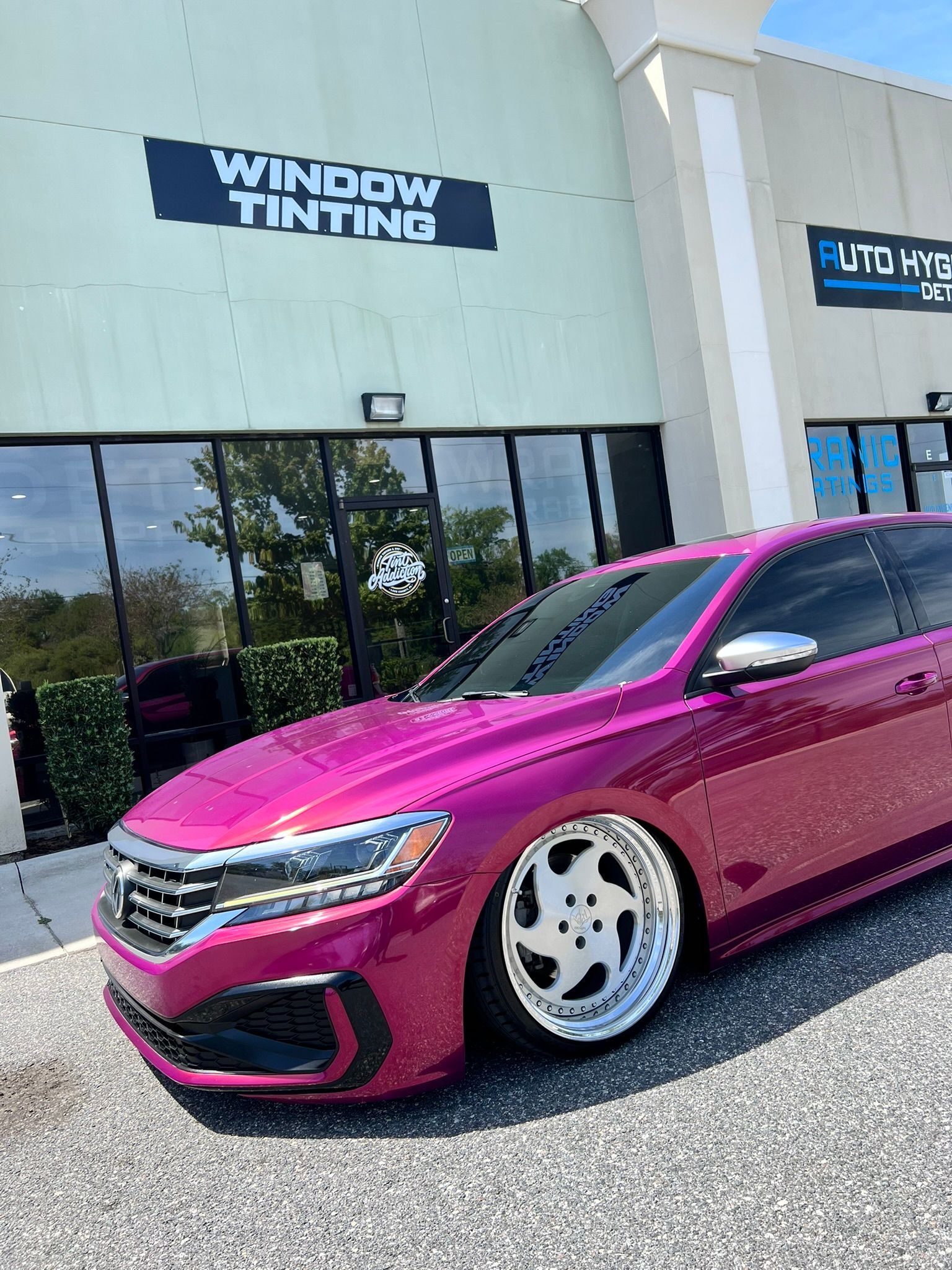 Magenta car in front of a window tinting shop.