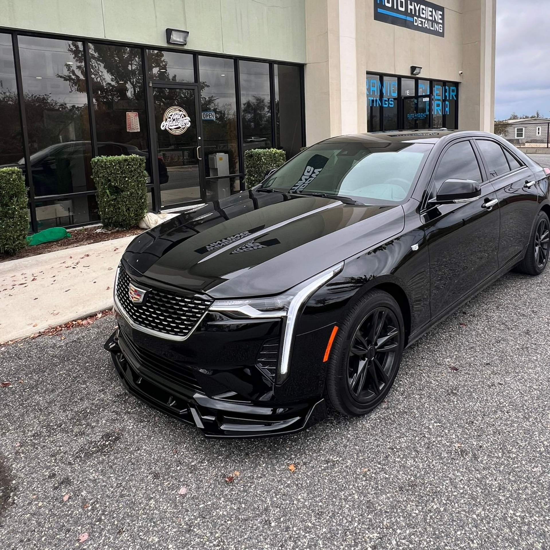 Black Cadillac sedan in front of a window tinting business.