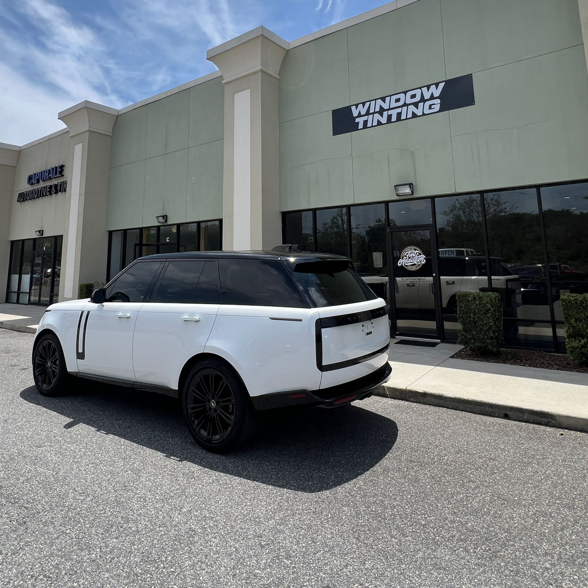 White Range Rover parked outside a window tinting business on a sunny day.