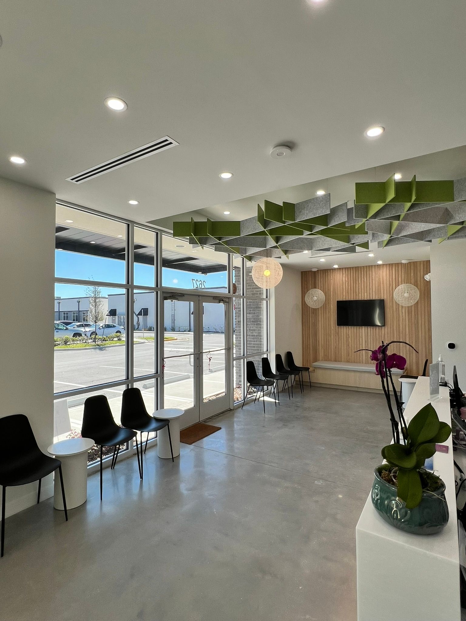 Modern waiting room with black chairs, large windows, and green ceiling decor.